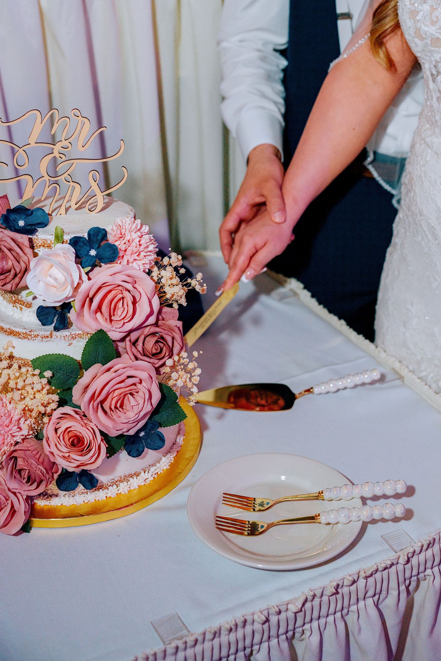 Bride and groom cutting a elegant three-tier wedding cake decorated with pink roses and a Mr & Mrs topper.