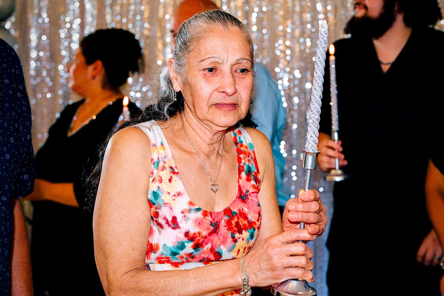 Elderly woman in floral dress holding a candle at a festive party event.