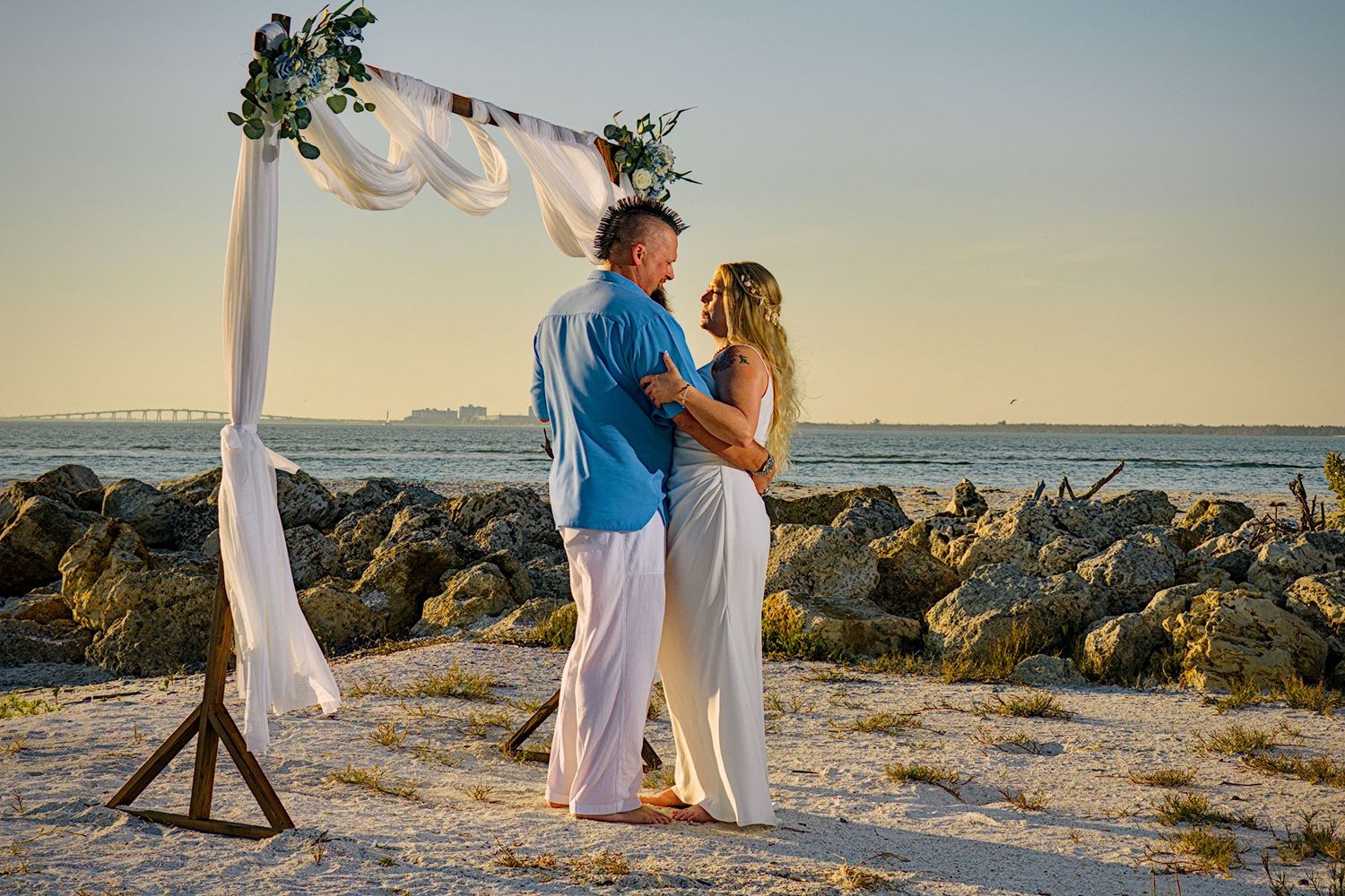 Romantic beach wedding couple poses at sunset among coastal rocks with ocean view.