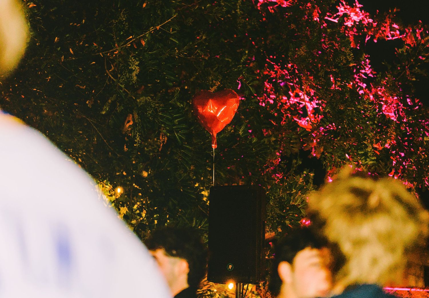 A heart-shaped balloon floats against a dark sky with red and yellow lights in the background.