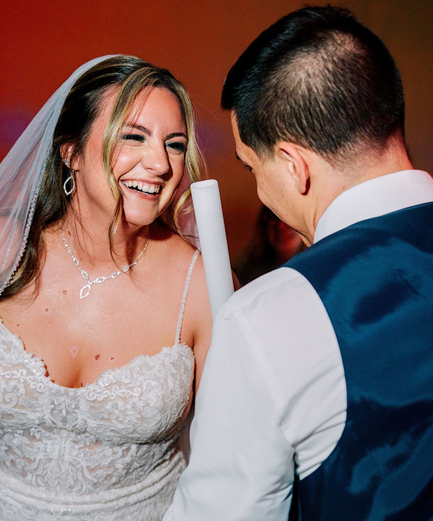 Radiant bride in lace gown laughs joyfully with groom during wedding reception dance.