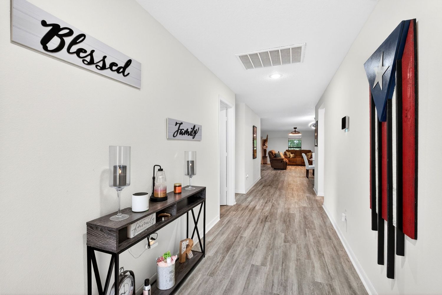 Bright hallway with wood-look floors, a console table, 'Blessed' wall sign, and Puerto Rican flag art leading to living area.