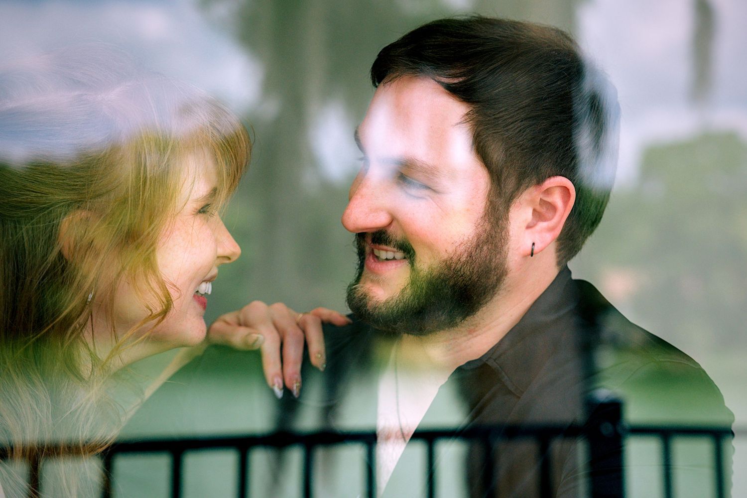 A happy couple smiling at each other through a window reflection outdoors.