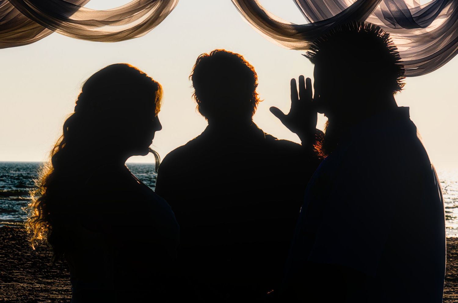 Silhouette of couple embracing against dramatic sunset sky at beach with waves crashing in background.