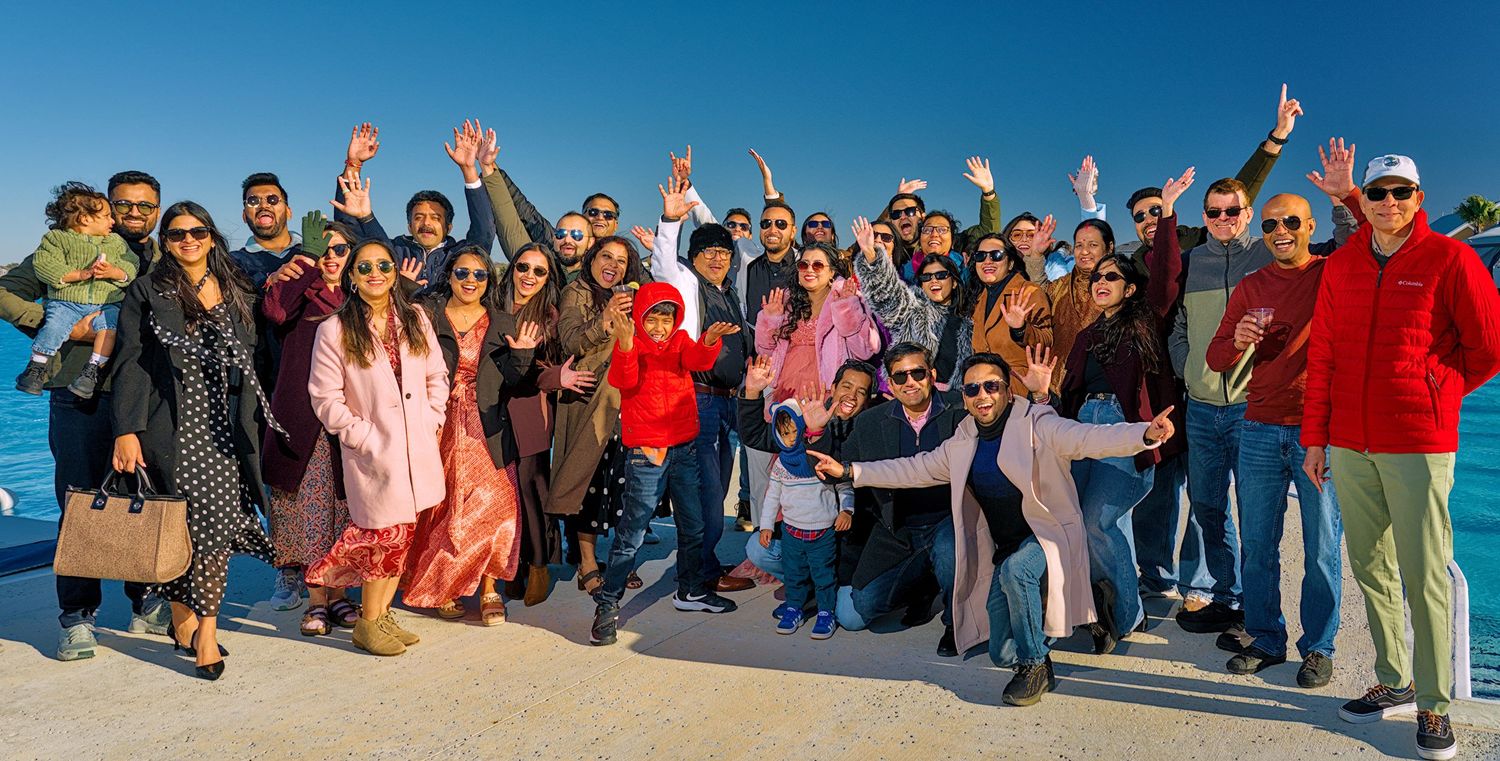 Large group of people sitting together outdoors on a sunny day with blue sky in the background.