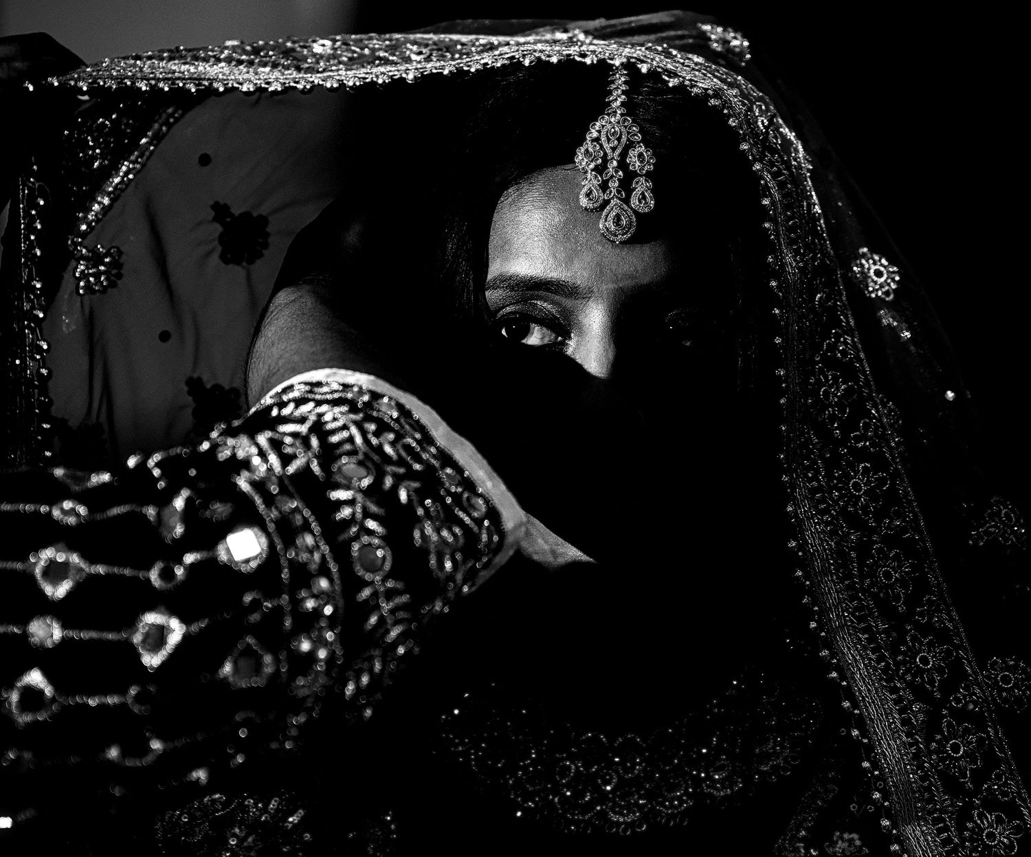 Black and white portrait of a bride in ornate jewelry and veil, showcasing traditional South Asian bridal attire.