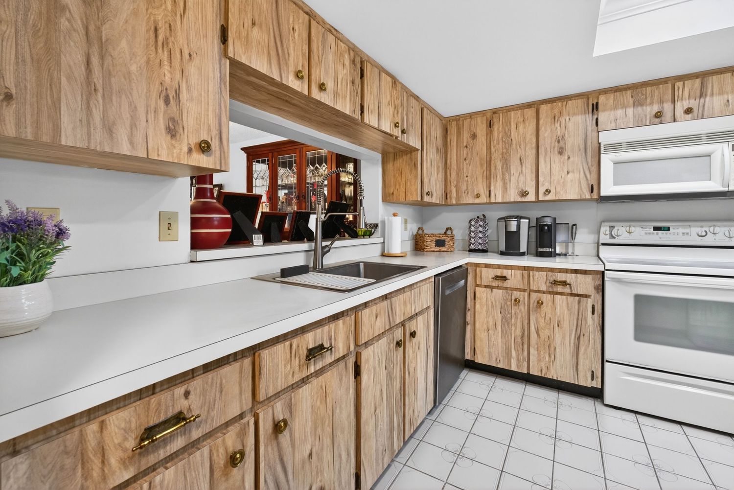 Bright kitchen with natural wood cabinets, white appliances, tile floor, and white countertops with a double sink.