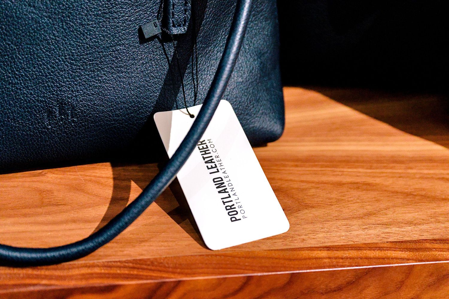 Black leather Portland Leather handbag with tag displayed on wooden surface.