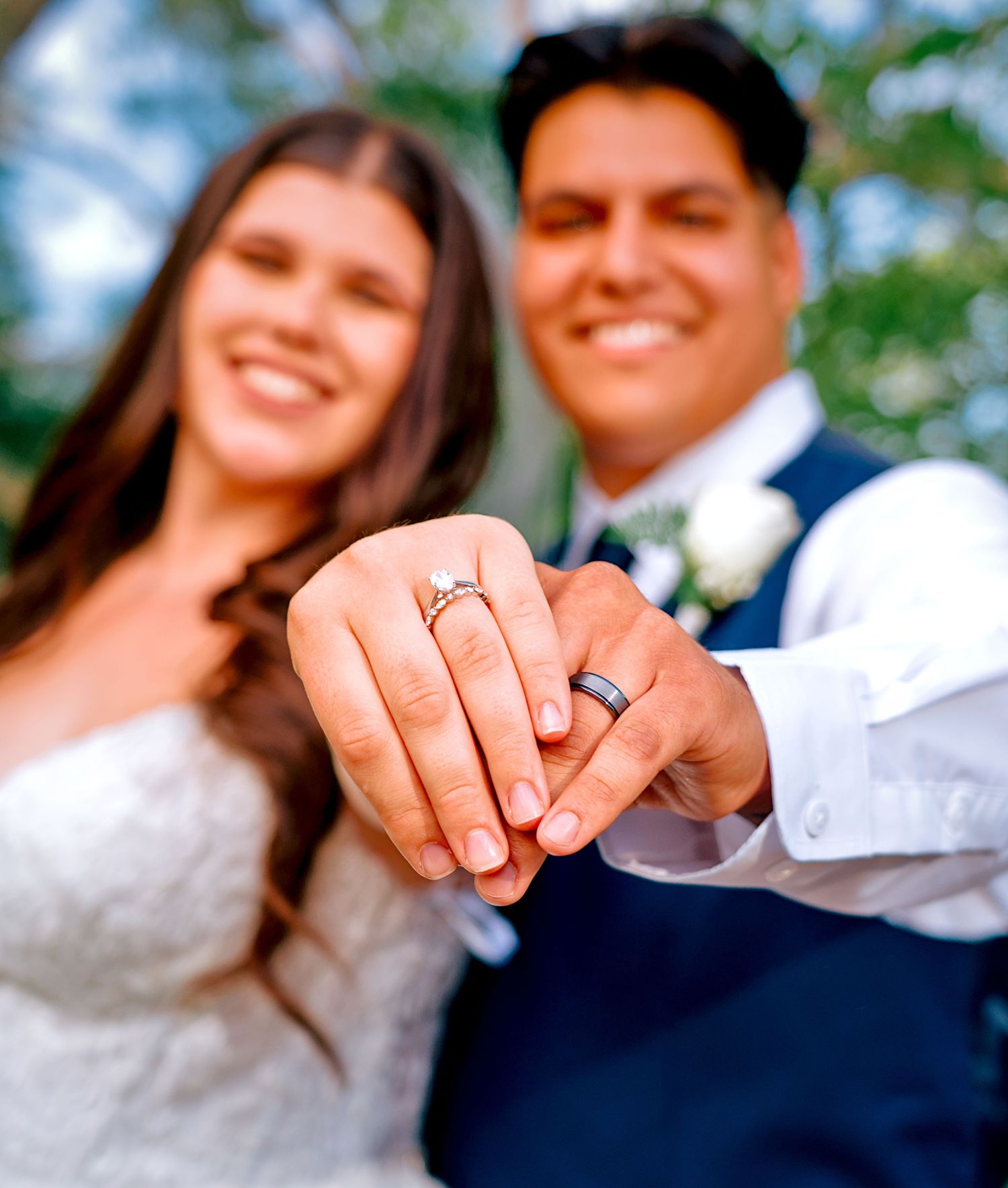 Smiling bride and groom showing off wedding rings on their fingers in a romantic outdoor ceremony photo.