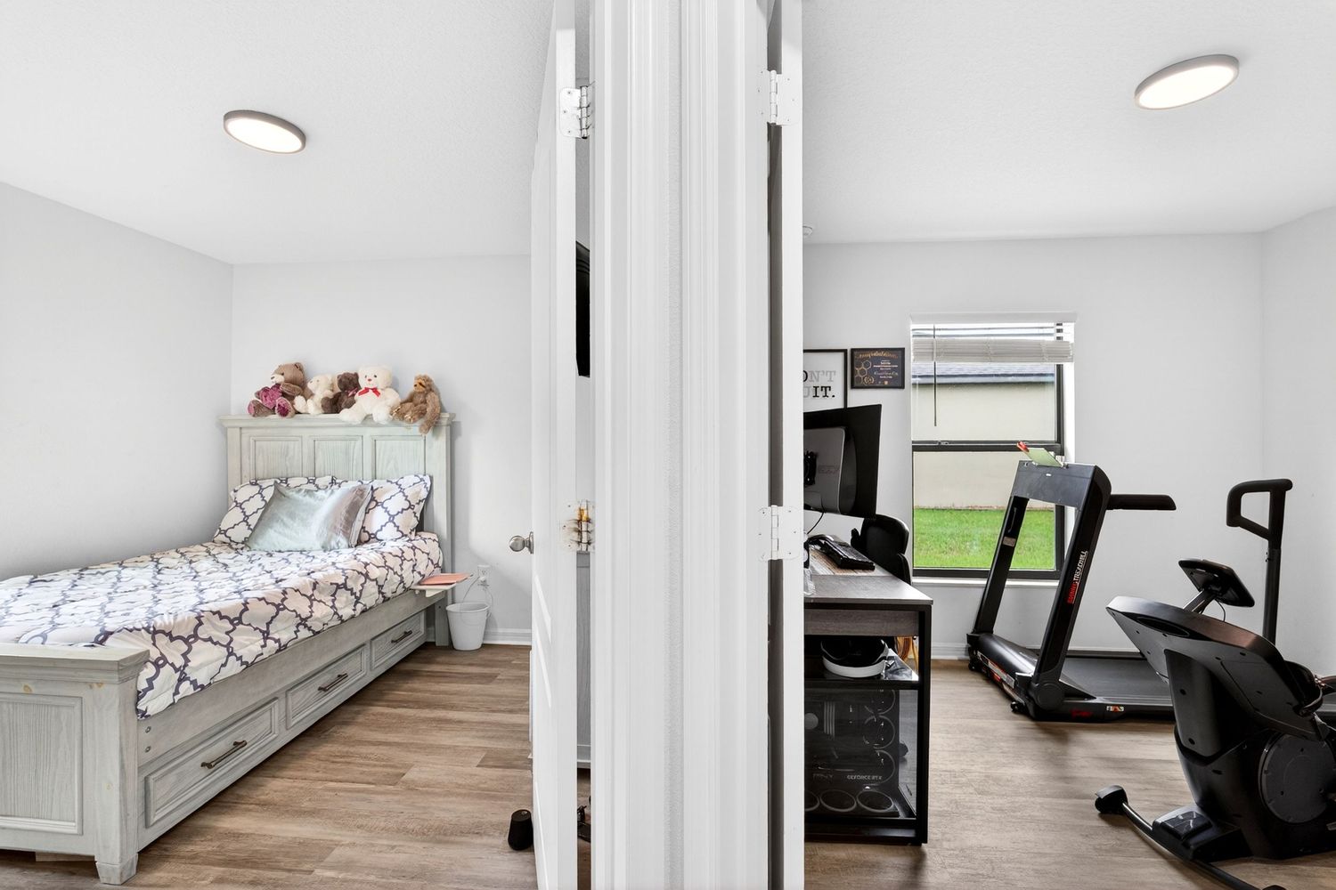 Doorway view showing a cozy bedroom with a wooden bed and a home gym featuring a treadmill and exercise bike.