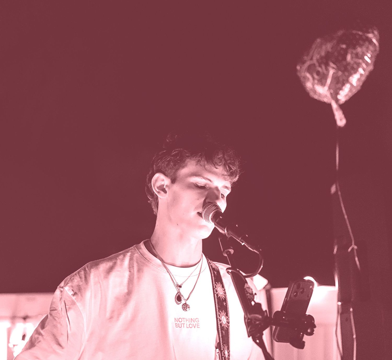 A performer singing into a microphone bathed in pink lighting during a concert.