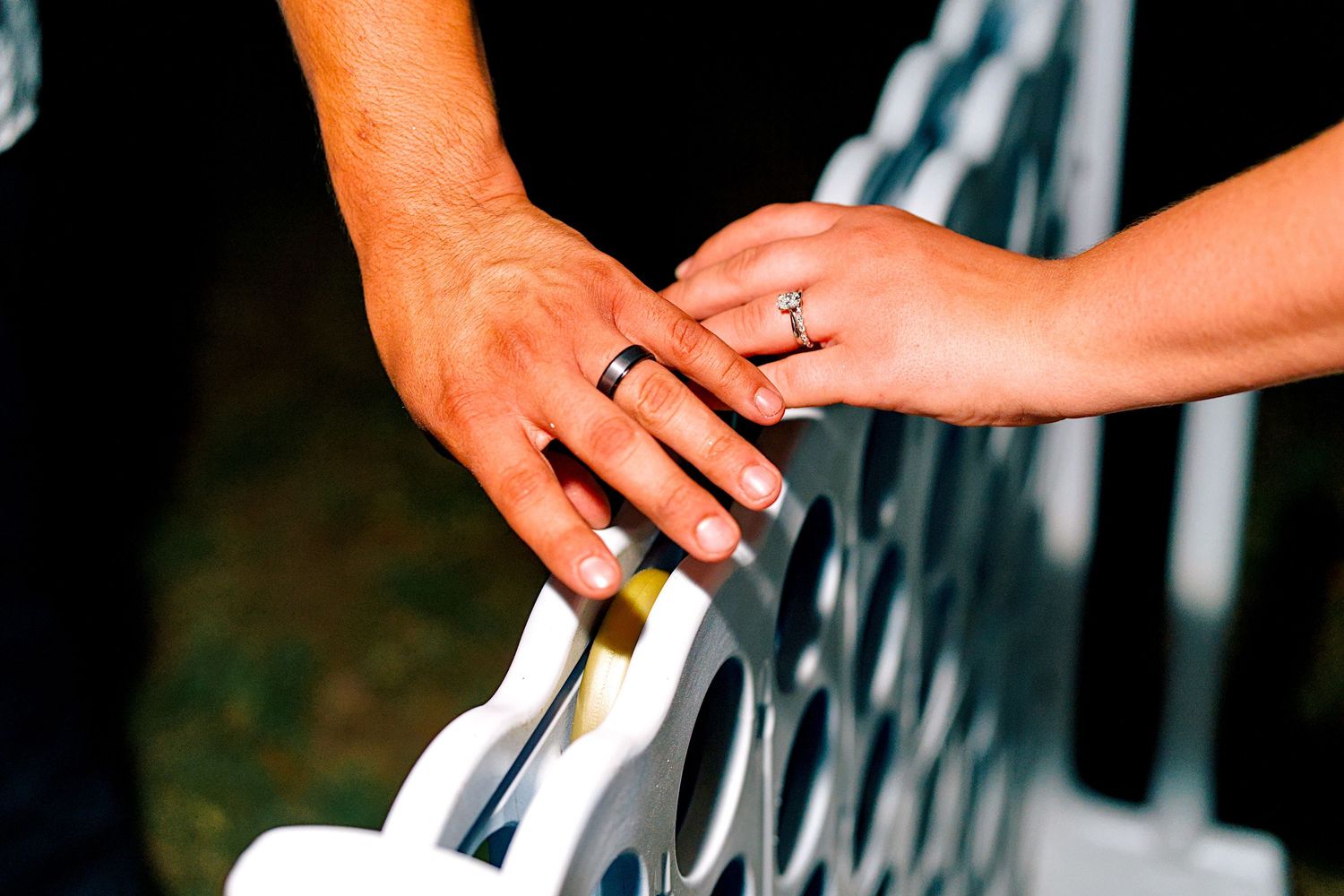 Close-up of bride and groom hands with wedding rings resting on white chair at wedding ceremony.