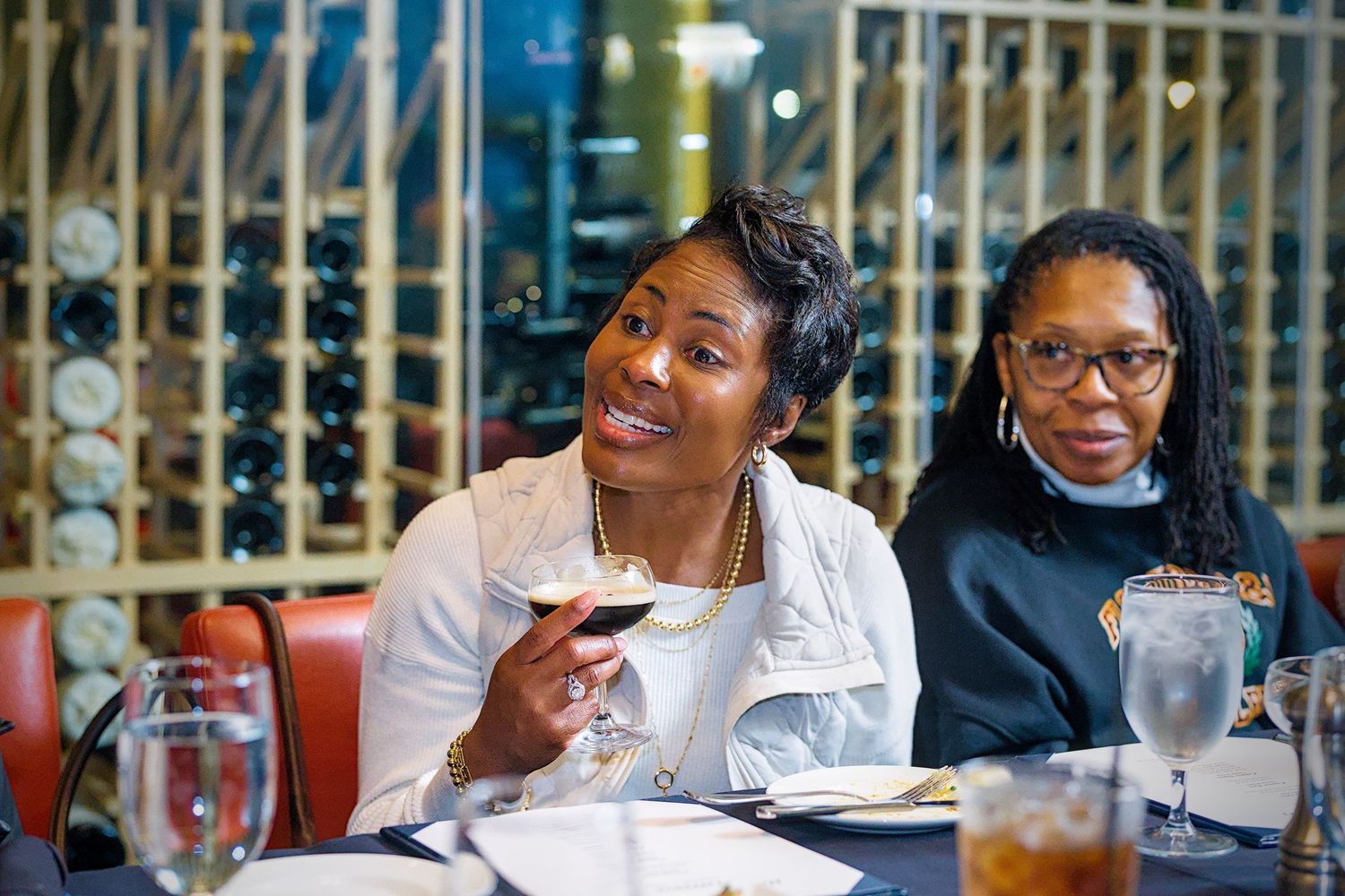 A group of people dining and socializing at a restaurant table with wine glasses and smiles.