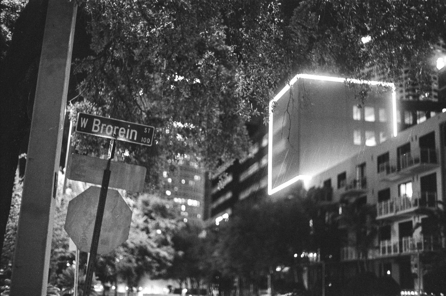 Black and white night photo of Brorein Street sign with illuminated buildings and trees in Tampa, Florida.