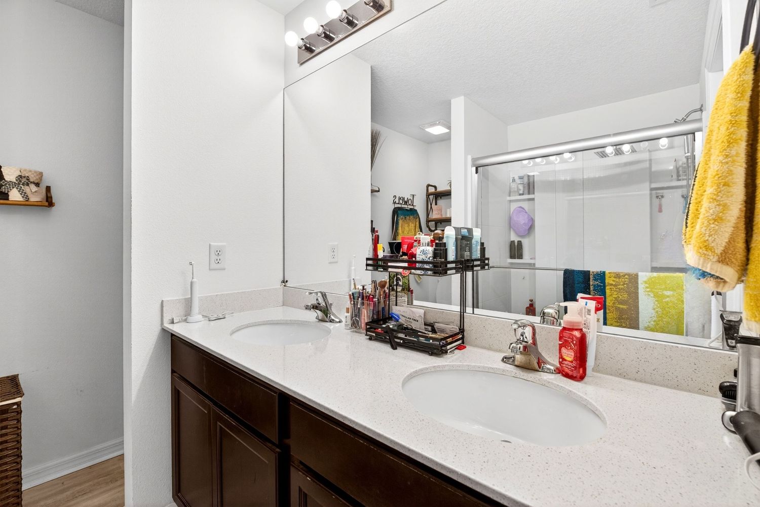 Modern bathroom with double sinks, dark wood vanity, quartz countertop, large mirror, and yellow towel accent.