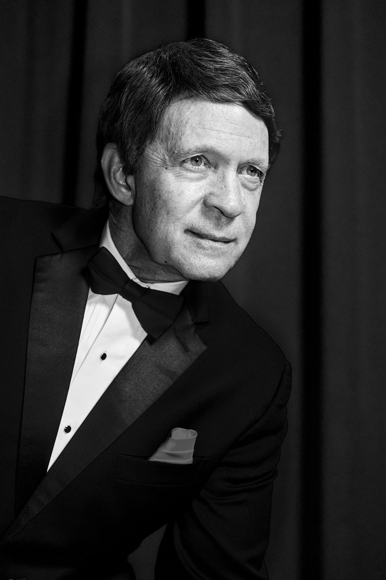 Elegant man in black tuxedo and bow tie poses for a classic black and white formal portrait photo.