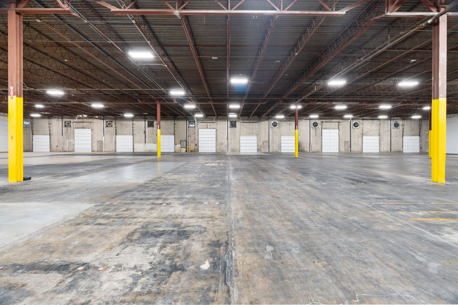 Empty industrial warehouse interior with concrete floor, yellow support columns, and overhead lighting.