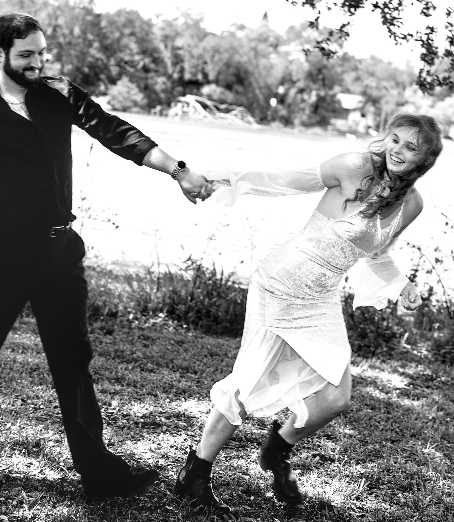 Black and white photo of joyful bride and groom dancing and spinning outdoors on their wedding day.