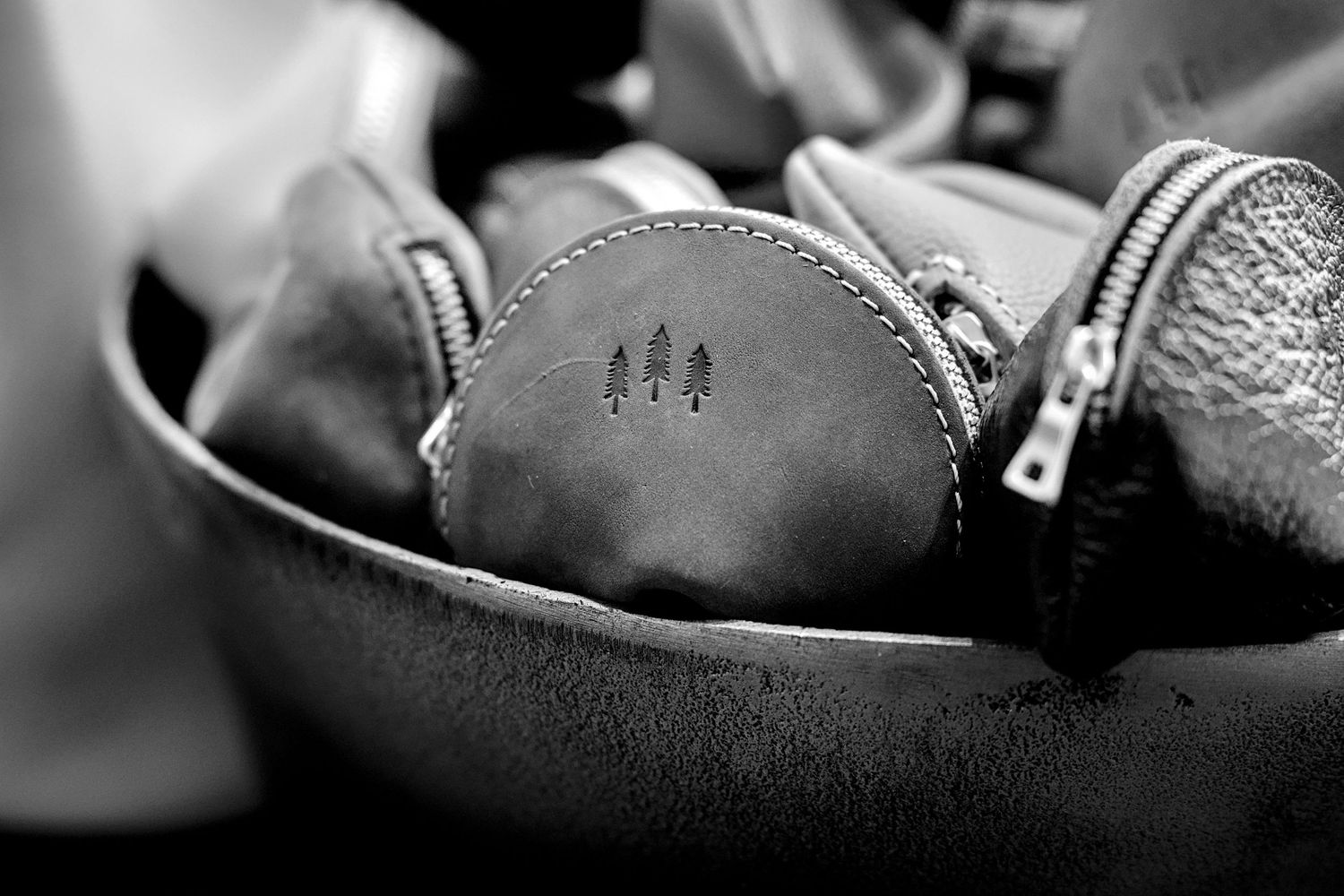 Close-up of a leather coin purse with tree logo embossed, nestled inside a gray suede bag with zippers.