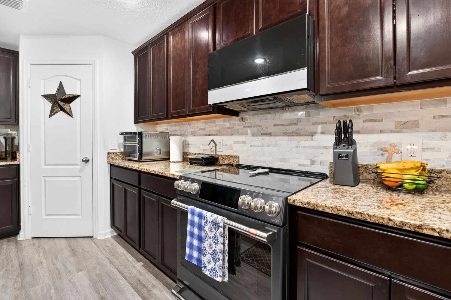 Modern kitchen with dark mahogany cabinets, granite countertops, stainless steel range, and elegant stone tile backsplash.