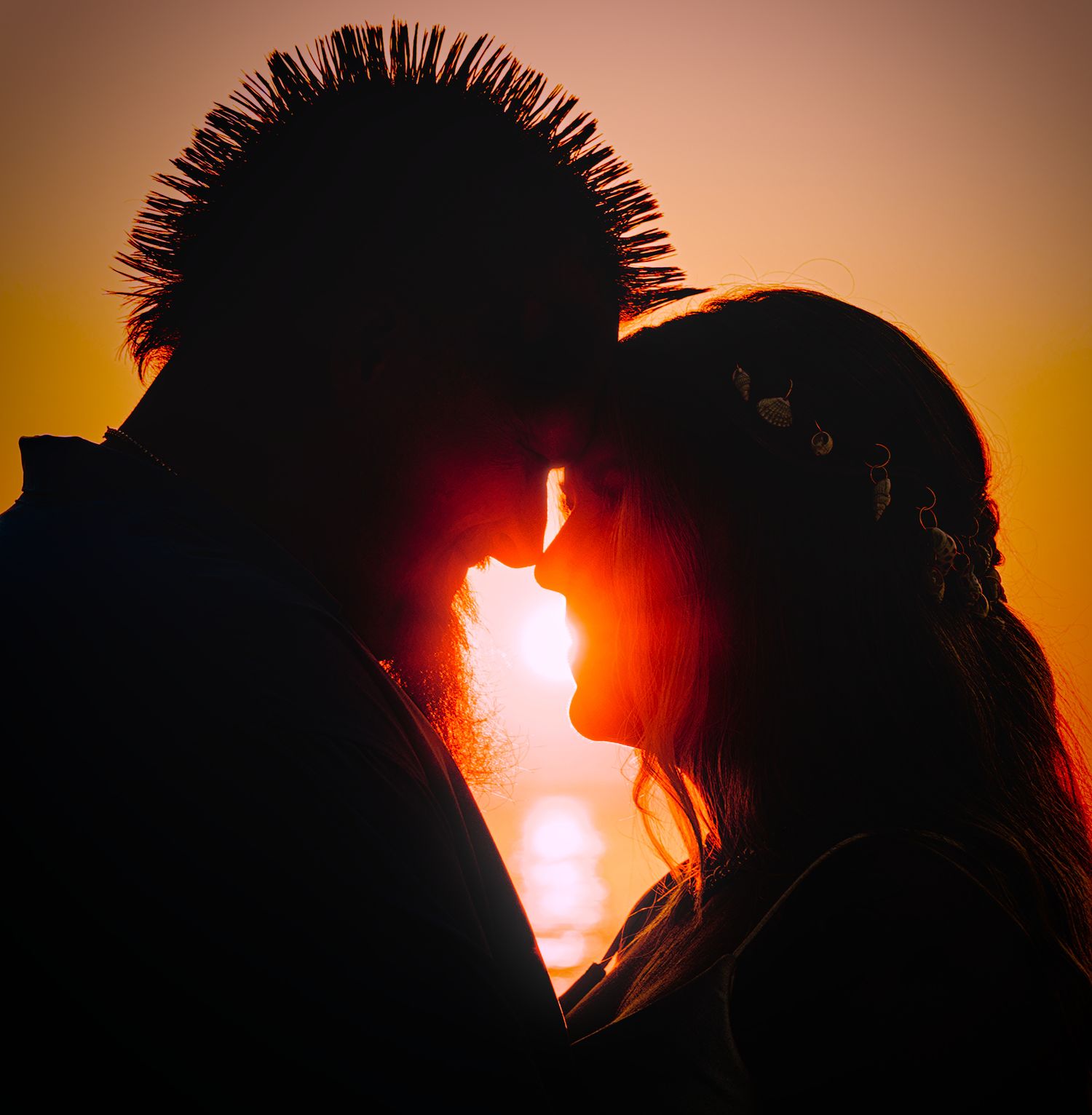 Romantic silhouette of a couple sharing a kiss at sunset with a warm golden sky backdrop.