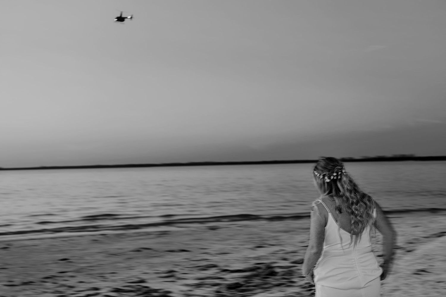 Black and white seascape with helicopter flying over calm waters.
