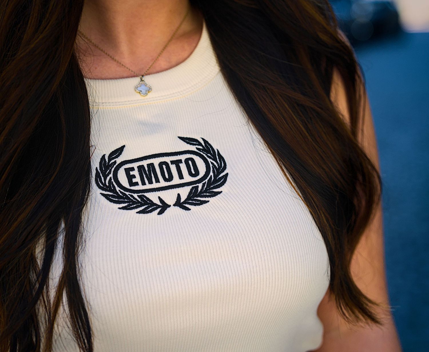 Close-up of a white ribbed tank top with a black EMDTD logo and laurel wreath design printed on the chest.