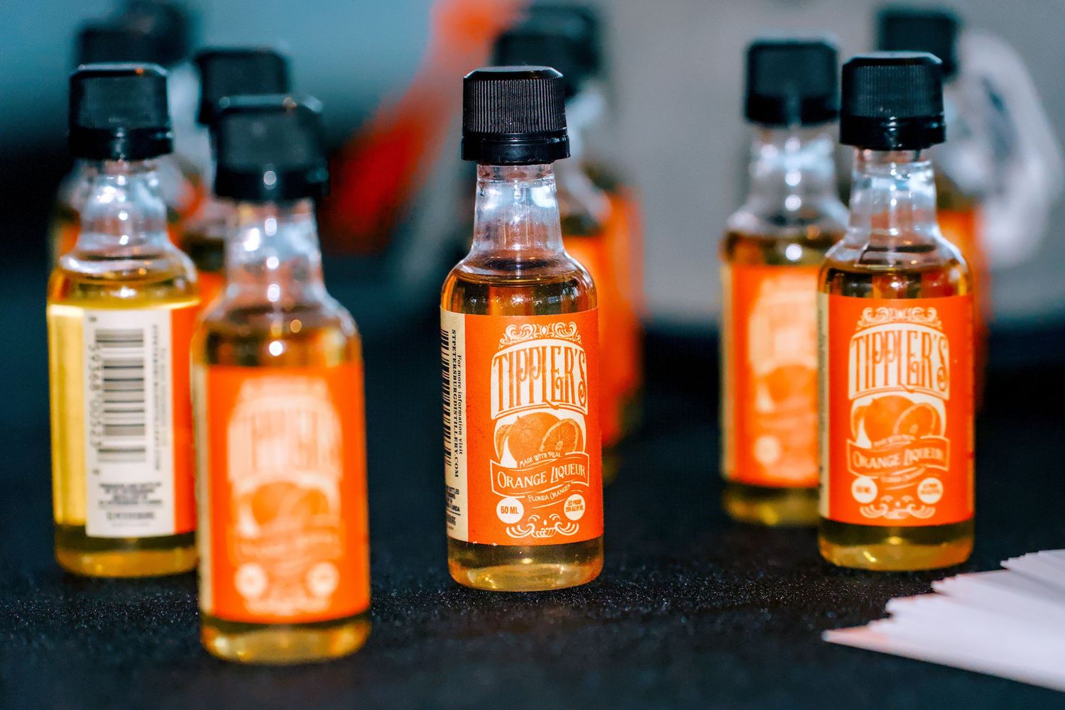 Small orange-labeled mini liquor bottles arranged on a dark surface at an event.