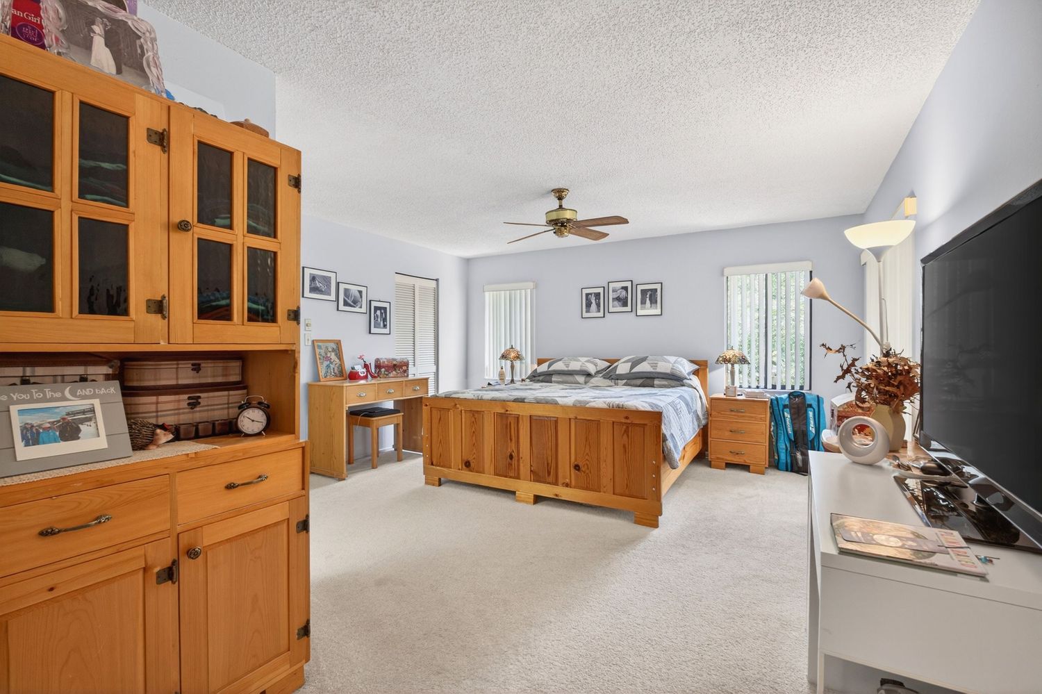 Spacious bedroom with pine wood furniture, ceiling fan, plush carpet, and a large wooden cabinet with glass doors.