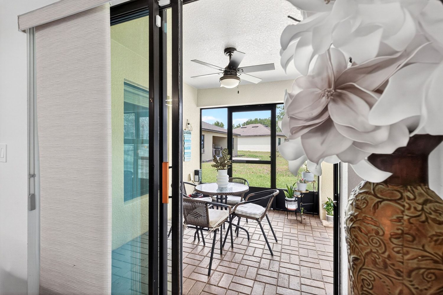 Sunroom with brick flooring, ceiling fan, sliding glass door, and outdoor dining area visible through large windows.