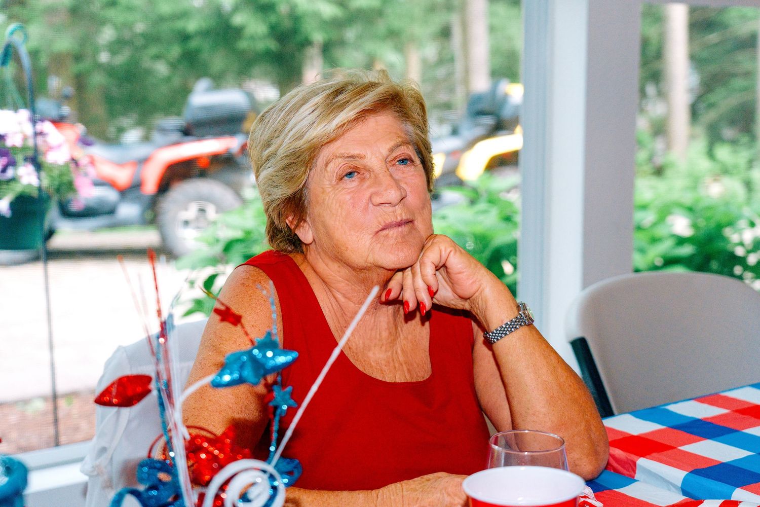 Older woman in red shirt sitting at patriotic red, white, and blue table at an outdoor Fourth of July celebration.