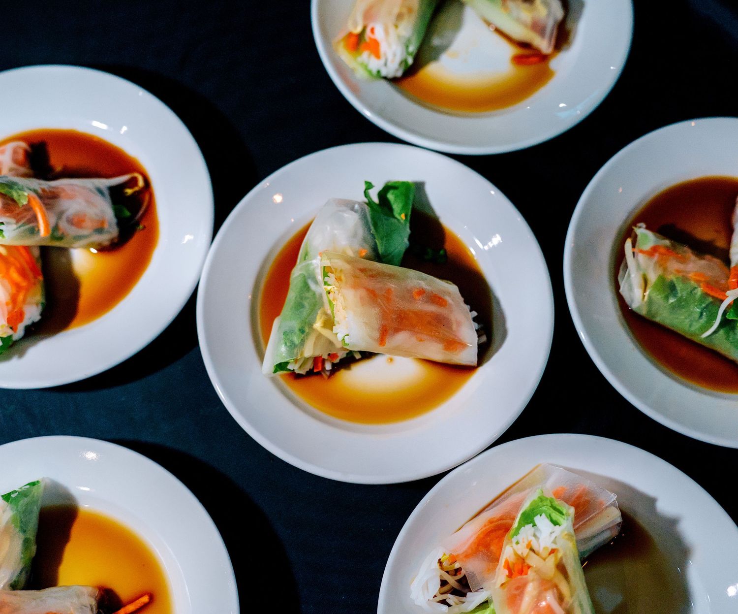 Six white plates of fresh Vietnamese spring rolls with shrimp, vegetables, and dipping sauce served at a catered event.