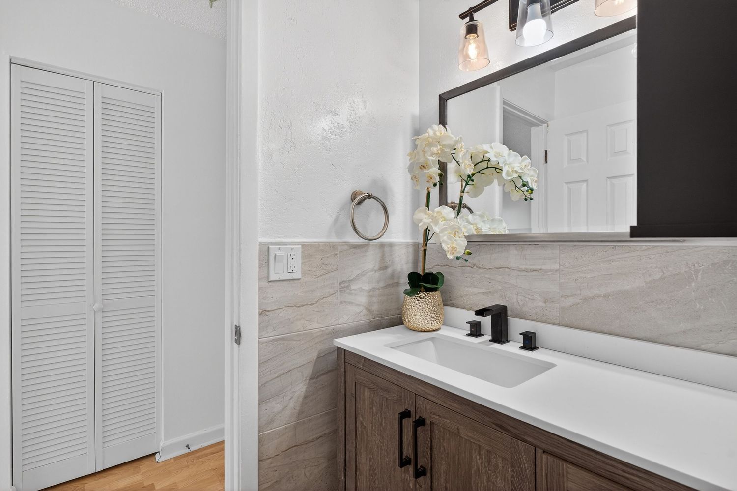 A bright and modern bathroom interior with white tiles, marble countertops, and contemporary black fixtures.