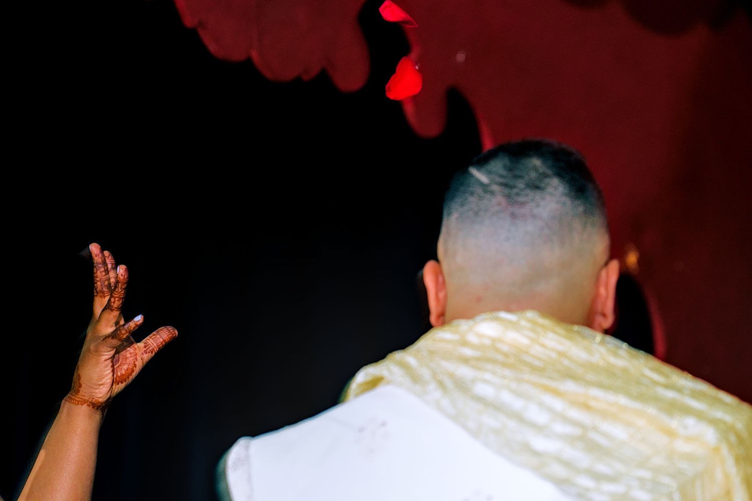 Person with shaved head in gold outfit raises henna-decorated hand at a vibrant nightclub event.
