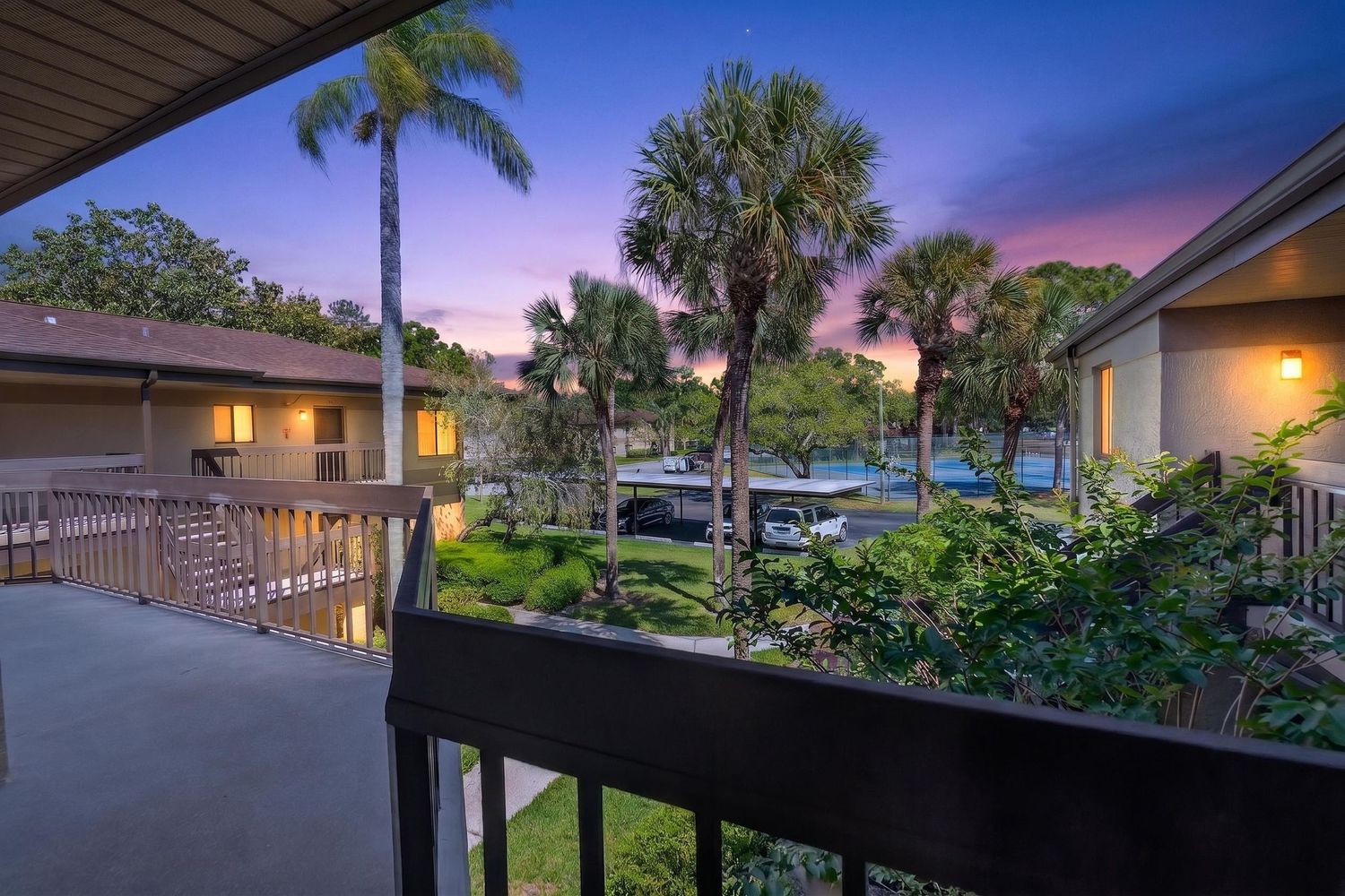 Twilight balcony view overlooking lush tropical landscaping with palm trees and a serene pool in a Florida residential community.