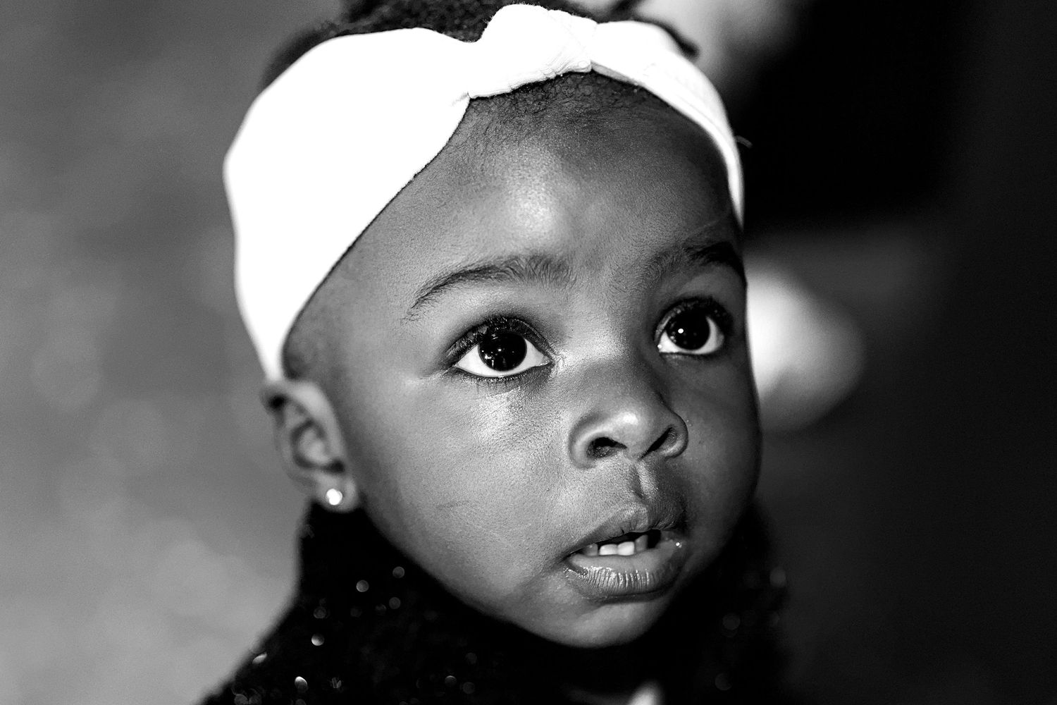 Black and white portrait of a young girl wearing a white headband, looking up with expressive eyes.