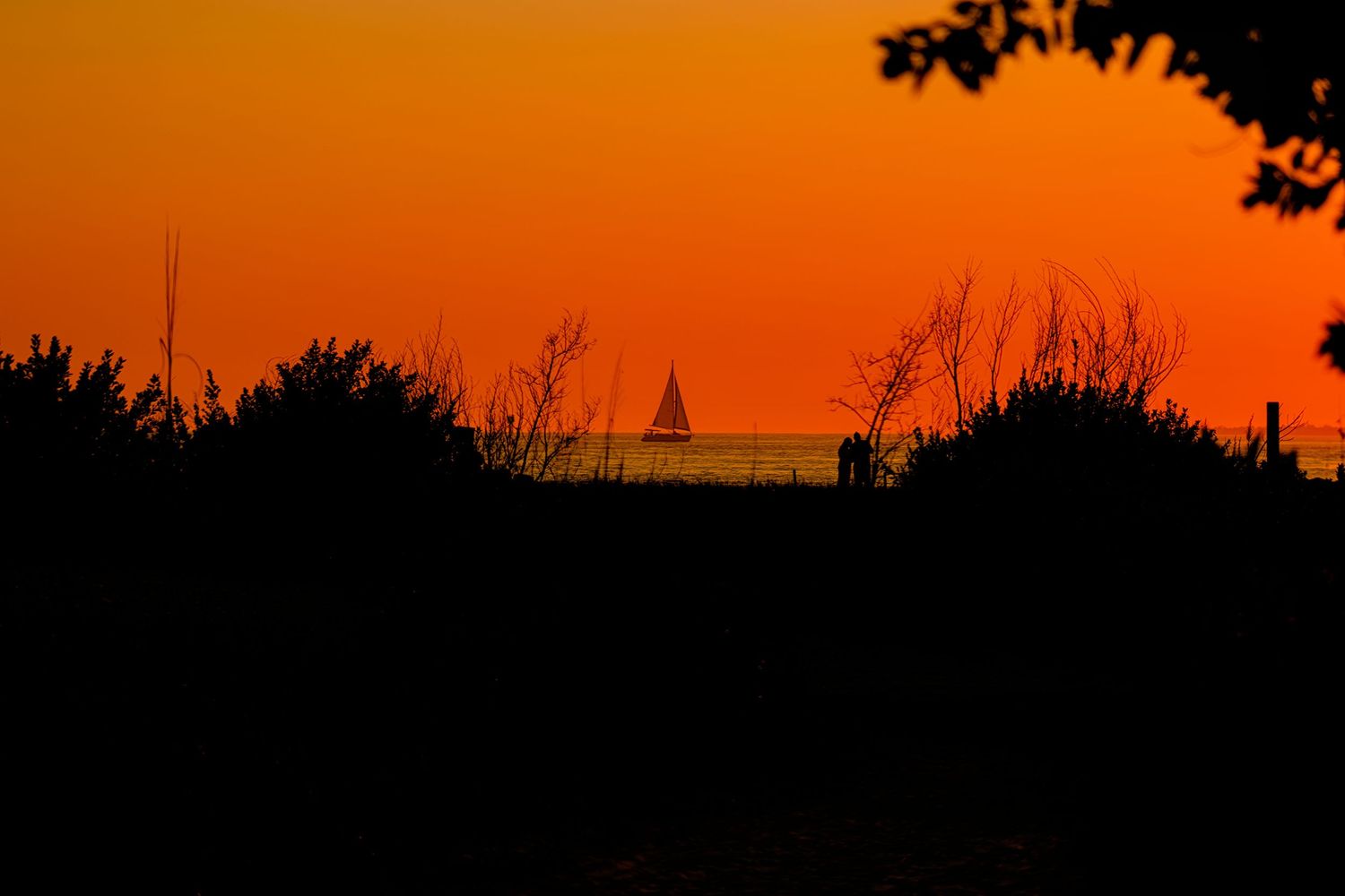 Dramatic orange sunset silhouette with sailboat visible on the horizon.