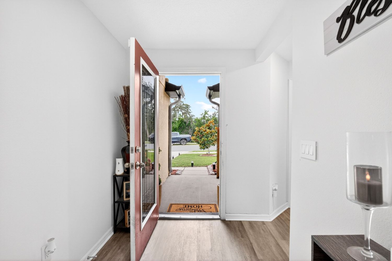 Open front door with wood flooring revealing a lush green yard in a bright, modern home entryway.