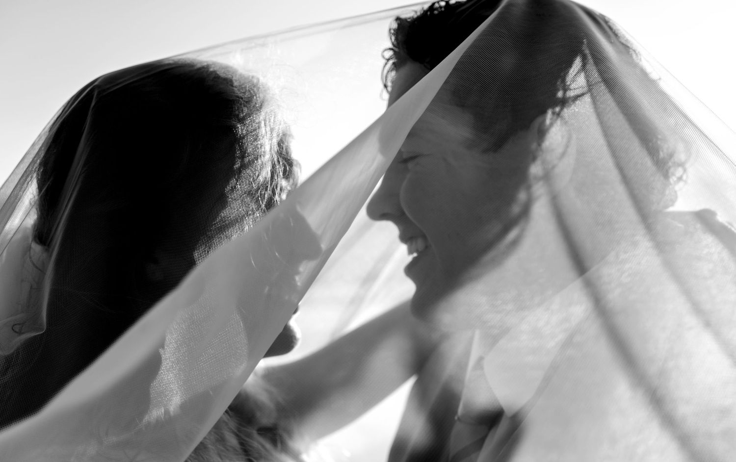 Black and white wedding photo of bride and groom sharing a romantic moment under a sheer veil.