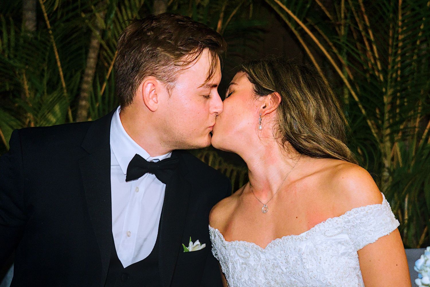 Romantic moment captured at an evening wedding with palm trees in background.