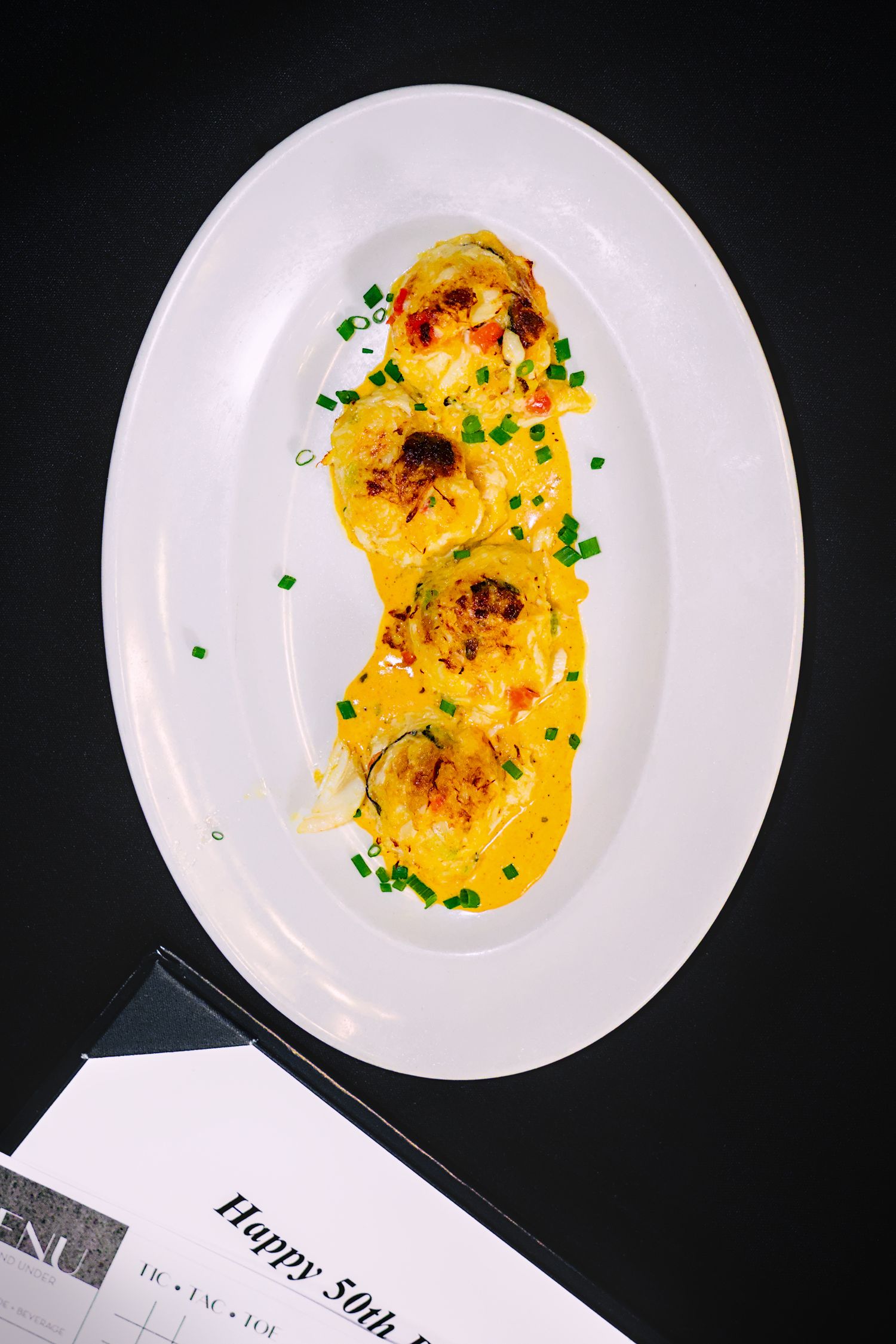 Elegant plated dishes with yellow sauce and garnish presented on white plates against a dark background.