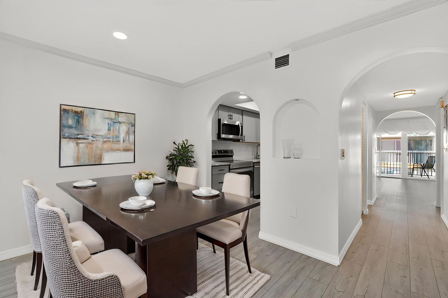 Modern dining area with dark wood table and beige chairs connects to hallway through elegant arched doorways.