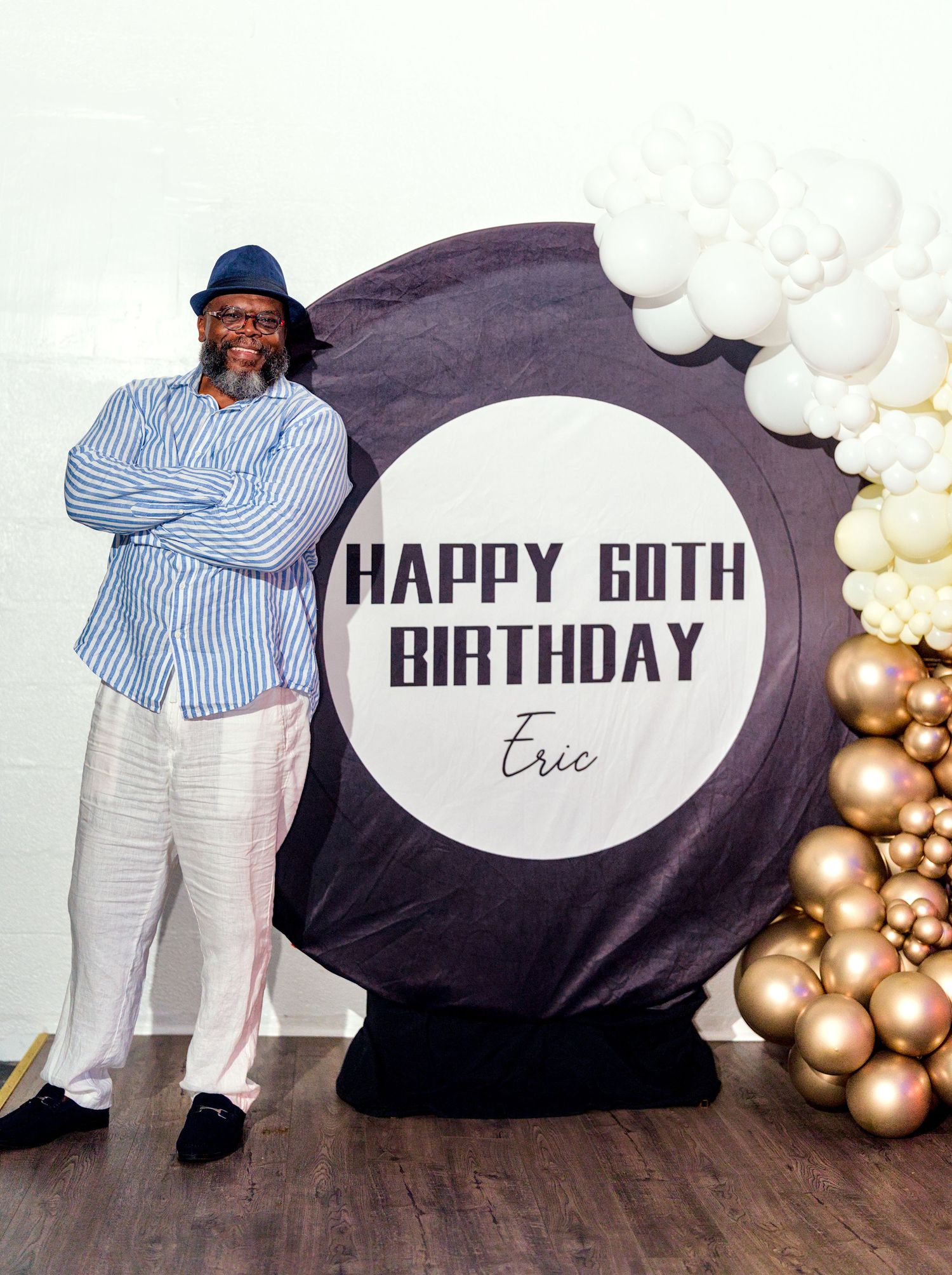 Man posing at a Happy 60th Birthday party for Eric, with balloon decorations and a large circular backdrop.