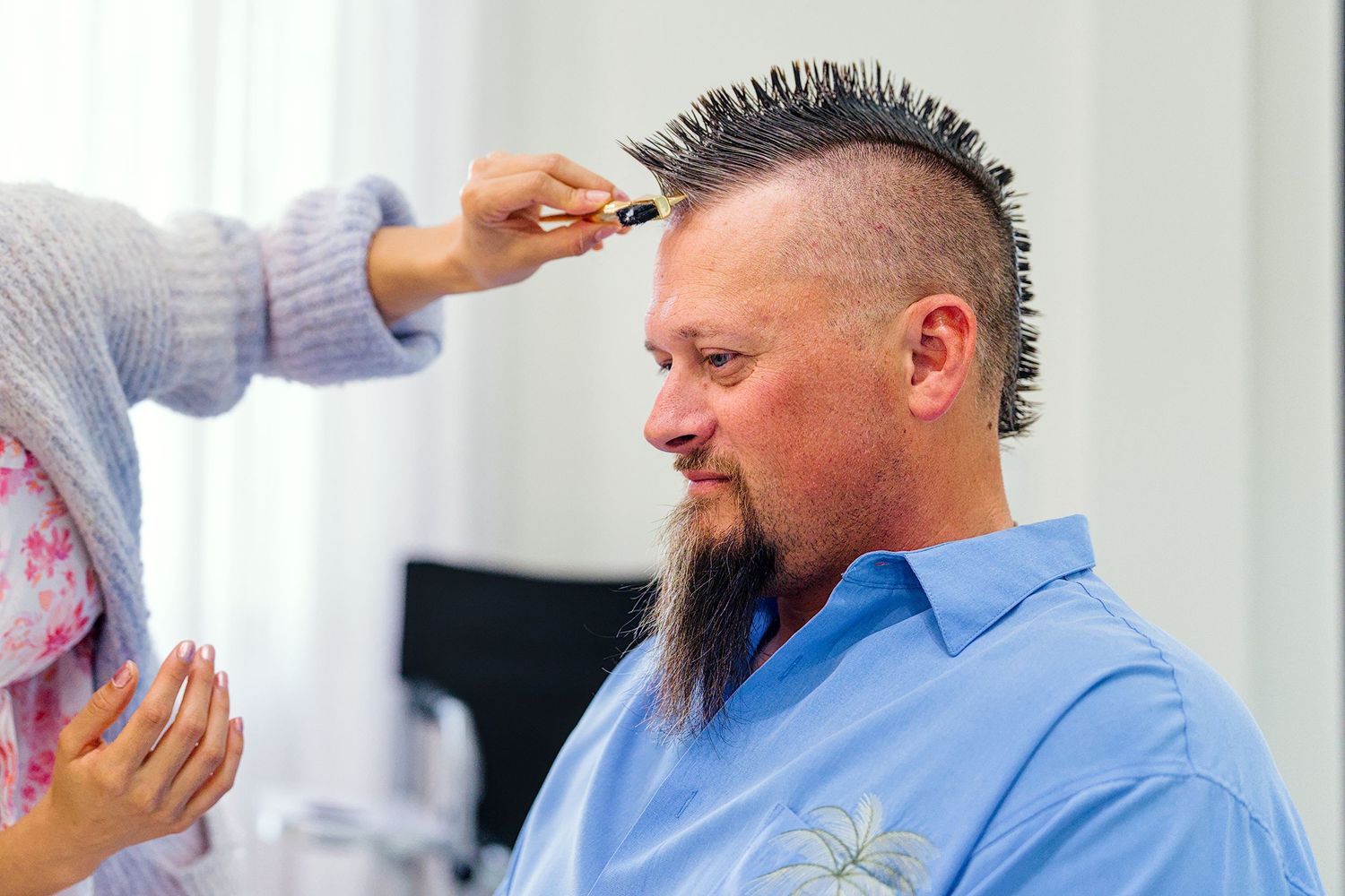 Stylists prepare groom's hair before wedding ceremony in bright indoor setting.