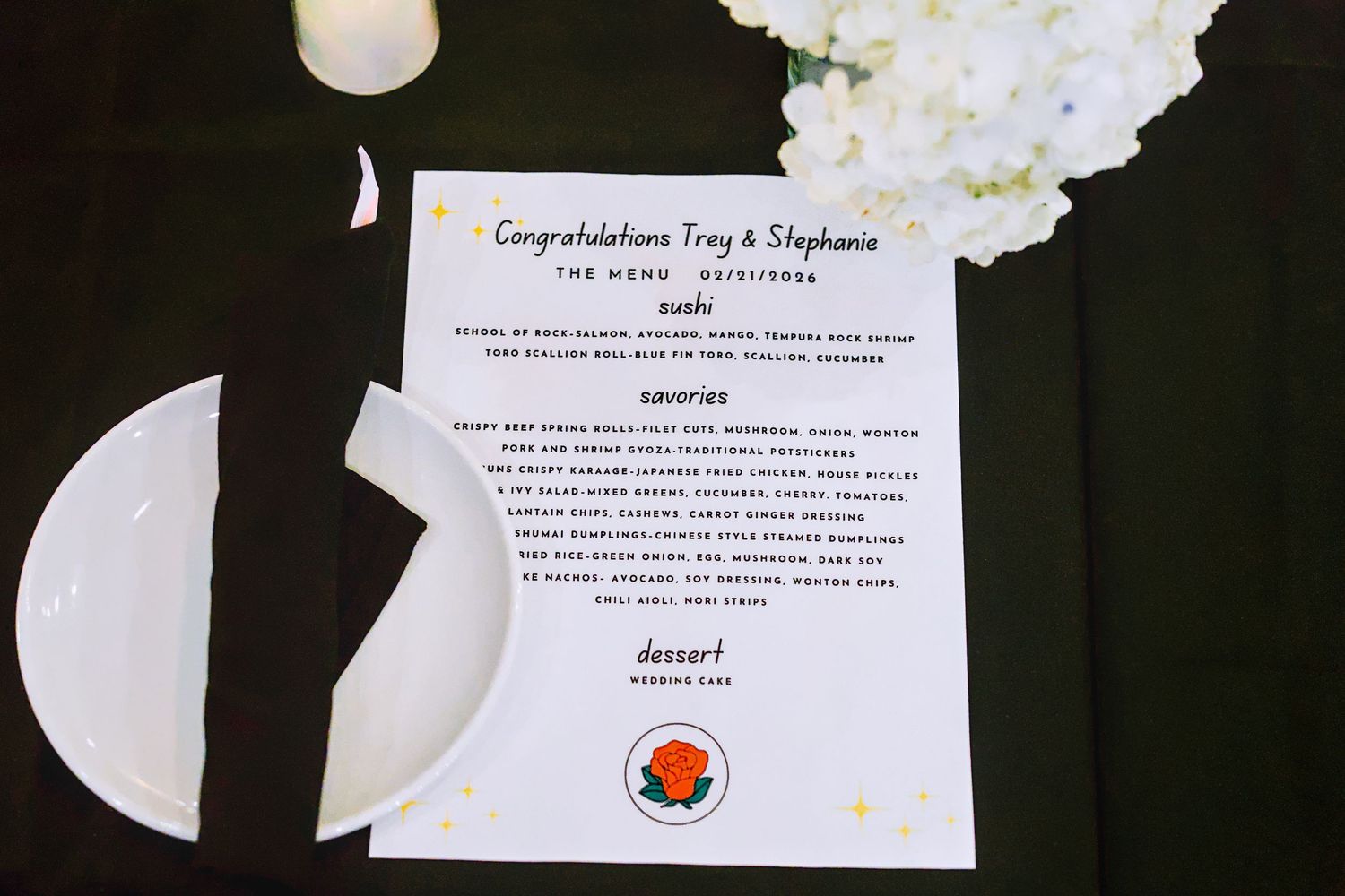 Wedding reception menu card congratulating Troy and Stephanie on a dark table with white floral arrangement.