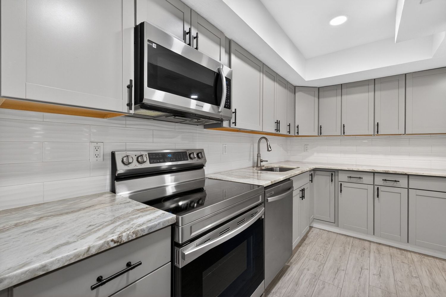 Modern kitchen with gray cabinets, marble countertops, stainless steel appliances, and white subway tile backsplash.
