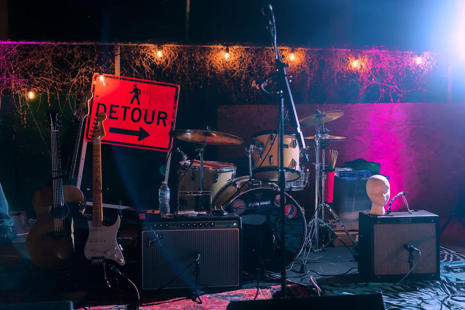 A detour sign on stage with musical equipment and blue-pink lighting.