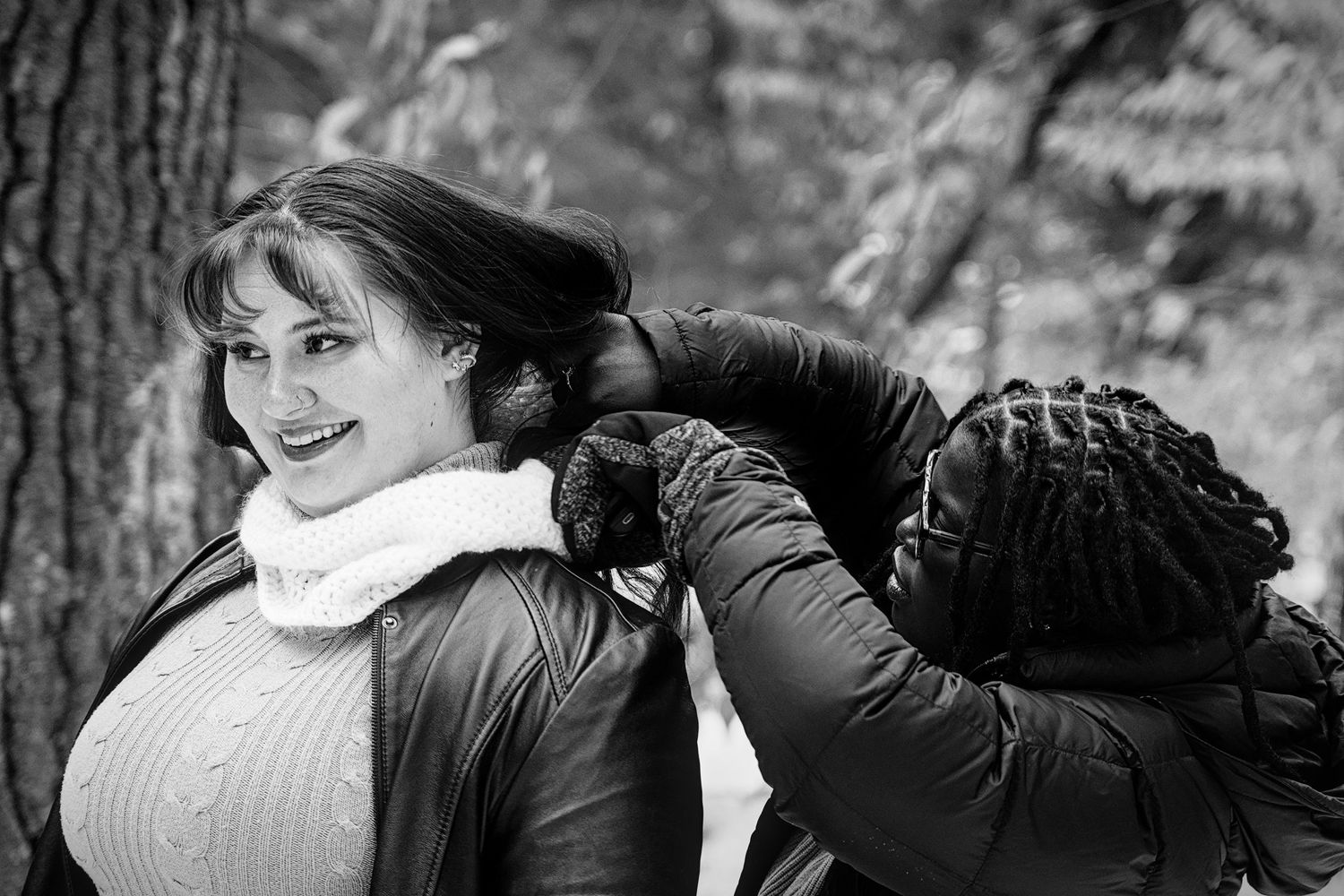 Black and white photo of two people in winter coats laughing together outdoors in a natural setting.