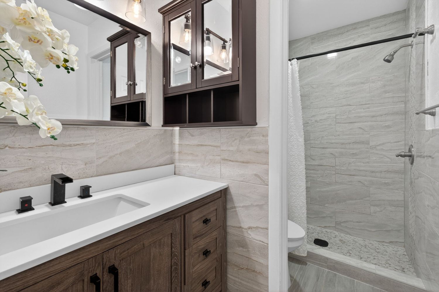 Modern bathroom design featuring white marble countertops, dark wood vanity, and matte black fixtures in a luxurious setting.