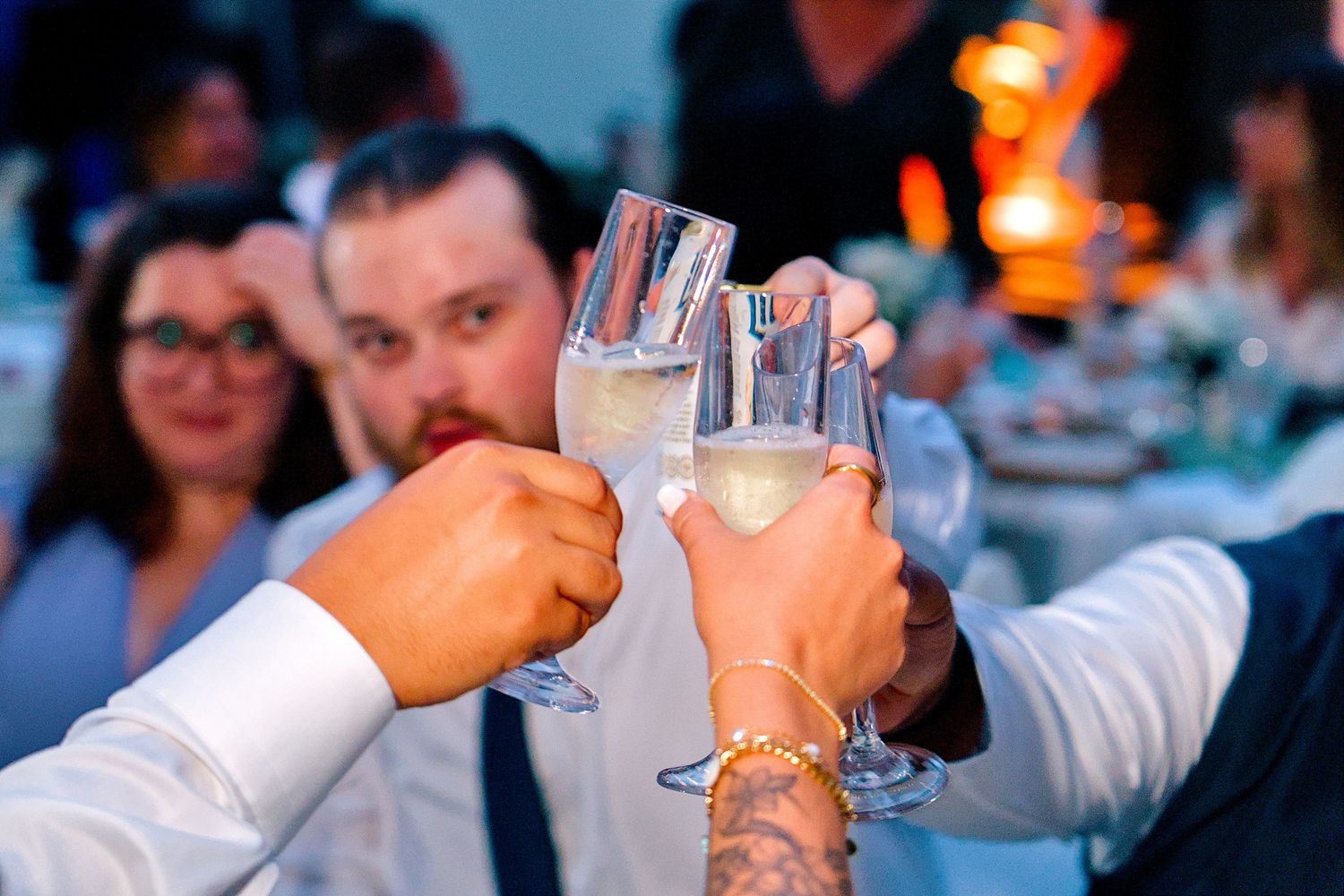 Wedding guests raise crystal champagne glasses in a celebratory toast at an elegant evening wedding reception.